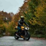 A motorcyclist in protective gear rides through a scenic autumn forest path., tags: und - pexel
