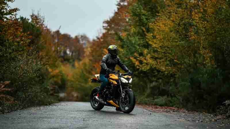 A motorcyclist in protective gear rides through a scenic autumn forest path., tags: und - pexel